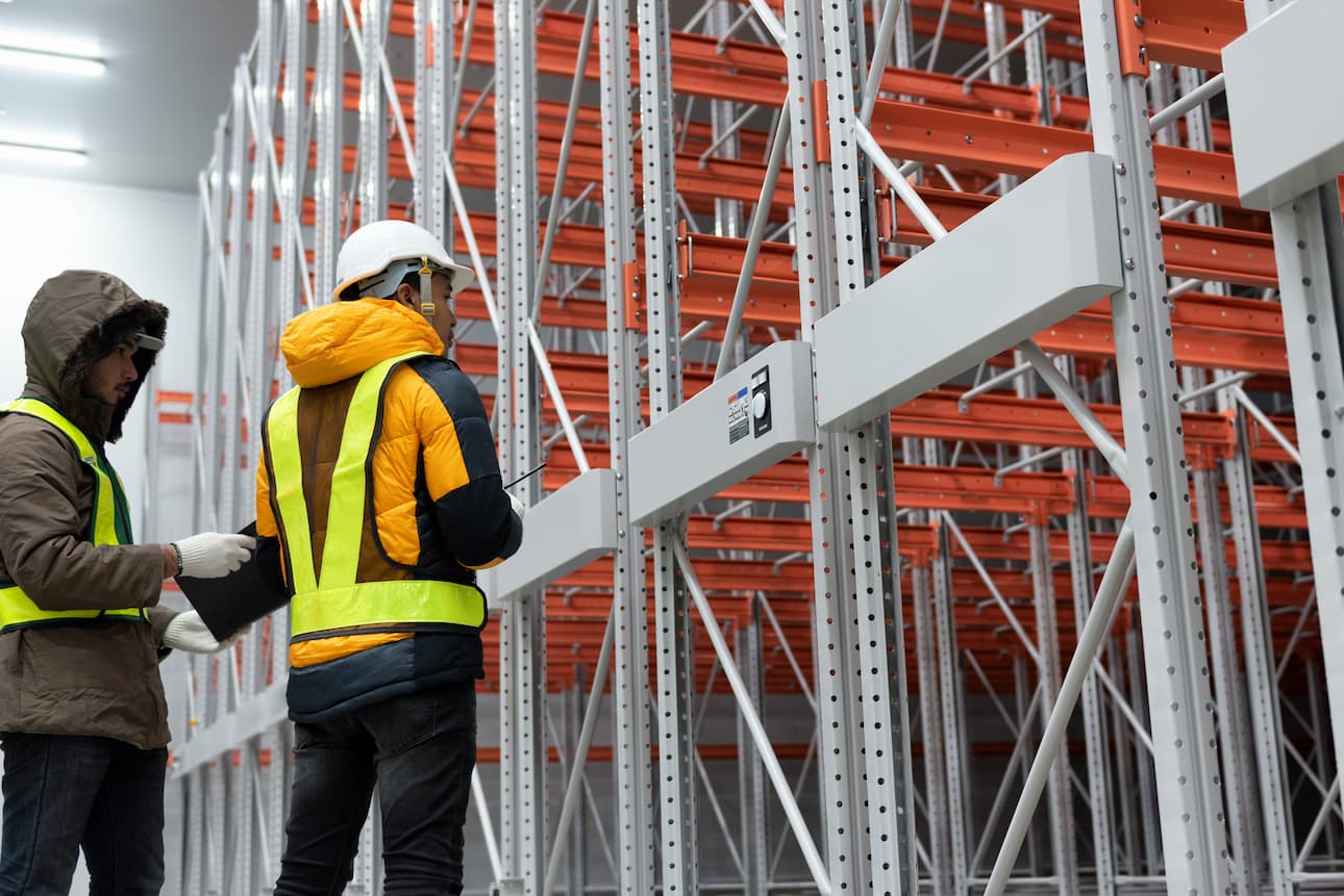 Interior de un almacén industrial con dos técnicos realizando una inspección técnica de estanterías (ITE)